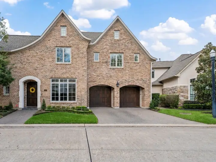 A two-story brick home with arched wooden garage doors